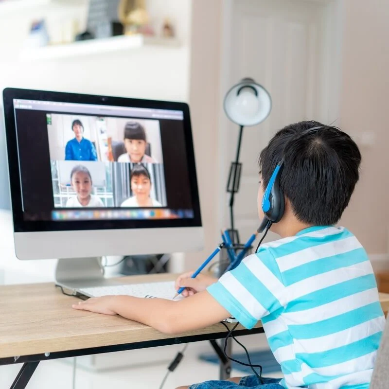 Child learning happily on a laptop in a virtual classroom setting.